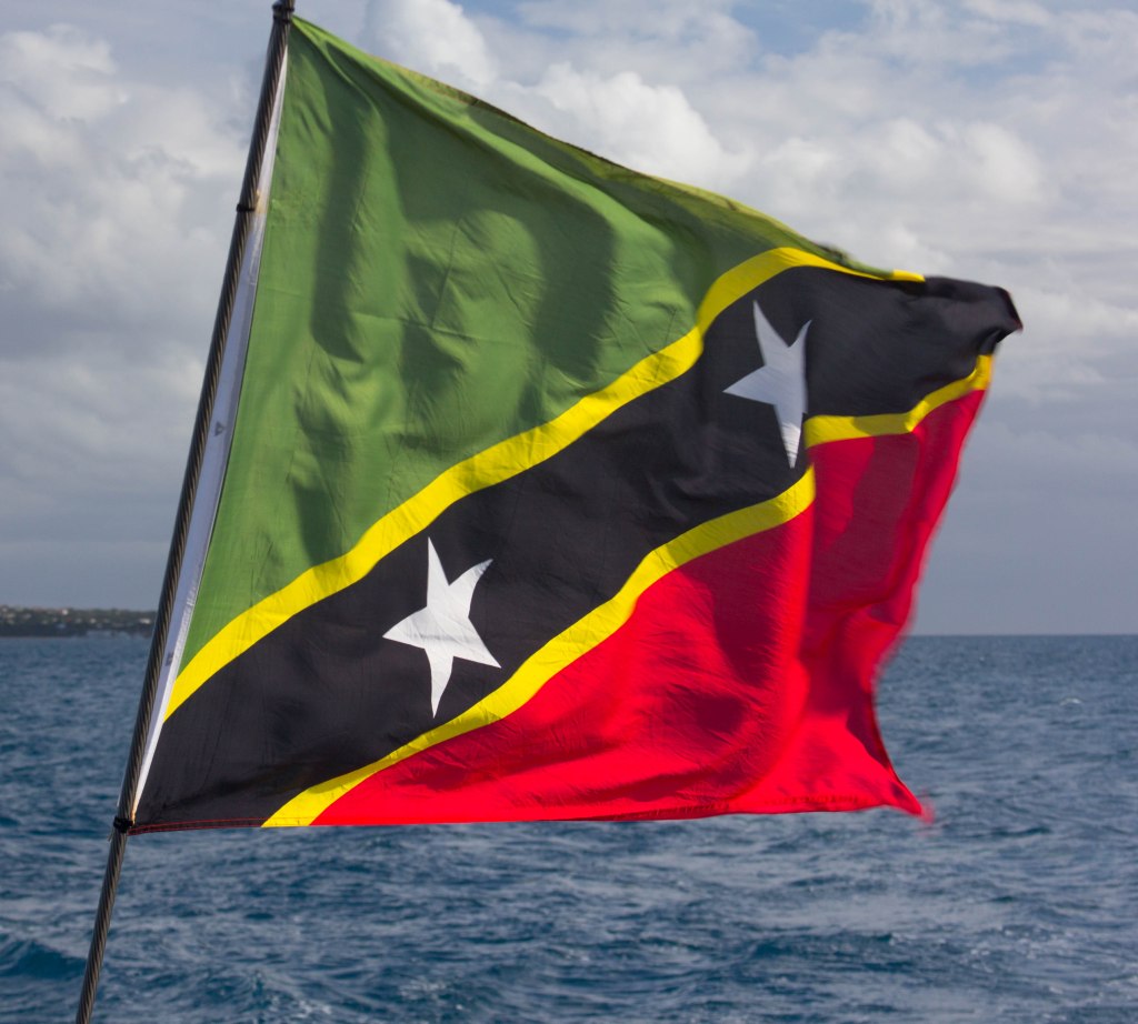 The National flag of St. Kitts & Nevis features green for fertile lands, yellow for year-round sunshine, black for the African heritage, and red for the struggle from slavery through colonialism to independence. It also displays two white stars on a black diagonal bar, symbols of hope and liberty.